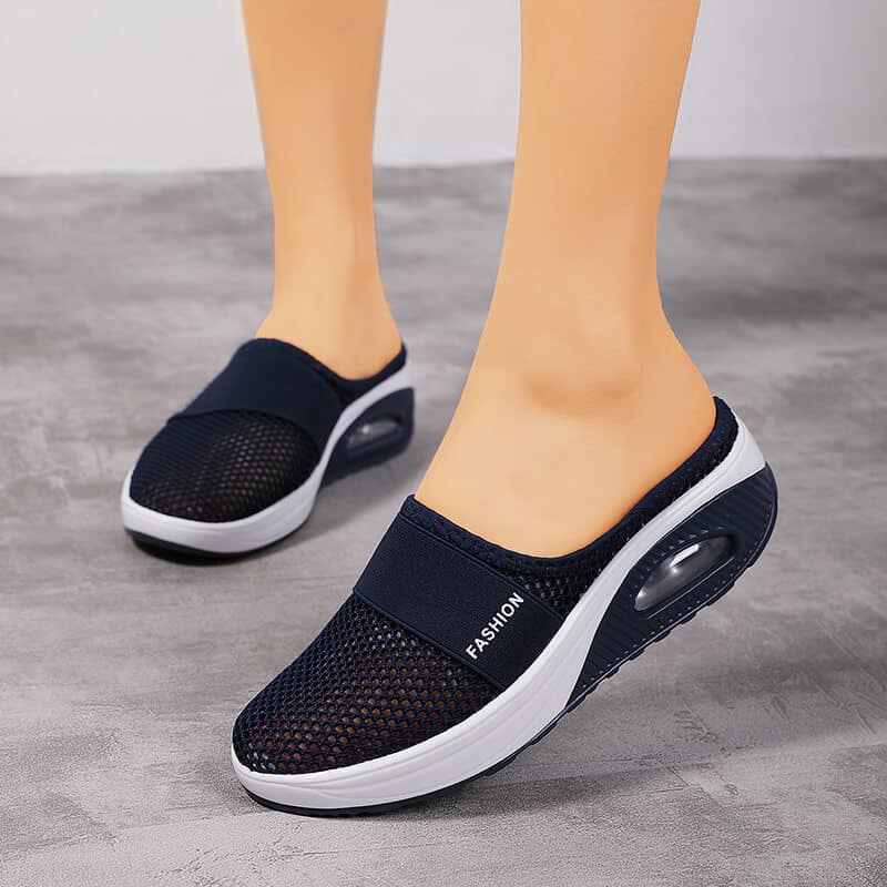 Letar du efter ett par ortopediska skor som är lika snygga som de är bekväma? Välj denna sportiga svartvita modell. Skorna är fotograferade på fötterna av en ung vit kvinna, på grått linoleum.